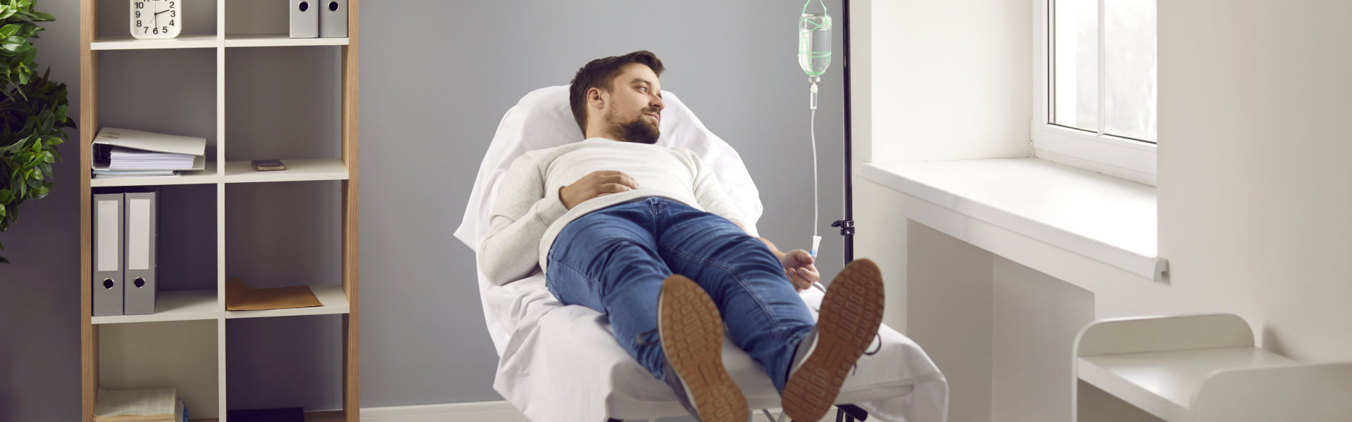 Young man attached to intravenous drip lying on bed